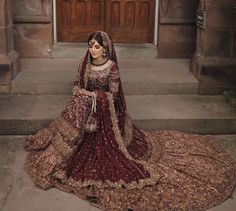 a woman in a red and gold bridal gown sitting on the steps outside an old building