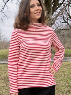 a woman standing in front of a tree wearing a red and white striped shirt with long sleeves