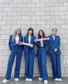 four girls in blue suits holding signs against a wall