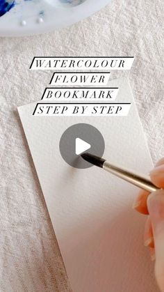 a person is using a marker to write on a piece of paper with the words watercolor flower / bookmark / step by step