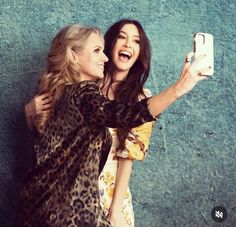 two women are taking a selfie with their cell phone while standing against a wall