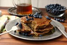 a stack of pancakes with blueberries and syrup on a plate next to silverware