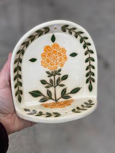 a hand holding a white and orange flower dish with green leaves on the rims