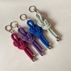 three key chains with different colored ropes attached to them on a white surface, the one in the foreground is an anchor