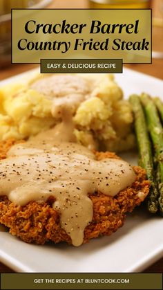 a white plate topped with meat covered in gravy next to potatoes and asparagus