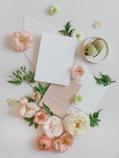 the wedding stationery is laid out with flowers and greenery on top of it