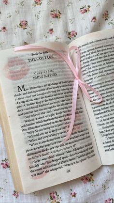 an open book with a pink ribbon on it