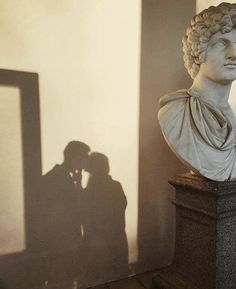 the shadow of a man and woman kissing in front of a statue