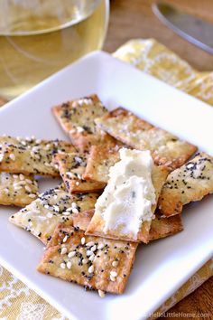 crackers with cheese and sesame seeds on a white plate next to a glass of wine