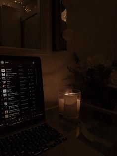 an open laptop computer sitting on top of a desk next to a candle and flowers