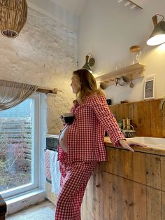 a woman standing at the counter in her pajamas and holding a glass of wine while looking out the window