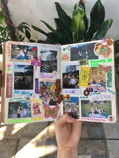 a person holding up an open book with pictures and stickers on it, in front of a potted plant