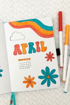 an open notebook with the word april written on it next to some crayon markers