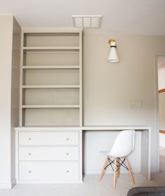 a white chair sitting in front of a book shelf next to a wall mounted light