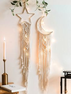 two wall hangings decorated with lights and greenery next to a lit candle on a table