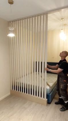 a man standing in front of a bed next to a wall with vertical blinds on it