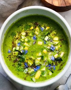 a white bowl filled with green soup and topped with blue flowers