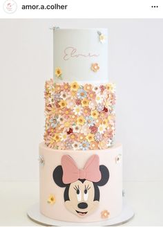 a three tiered cake decorated with flowers and mickey mouse's head on top