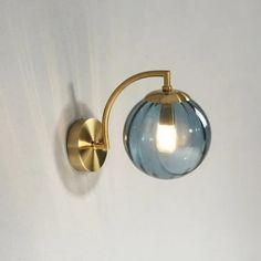 a wall light with a blue glass ball on the side and a gold metal arm