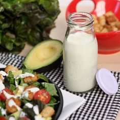 a salad with dressing in a glass jar next to it on a checkered table cloth