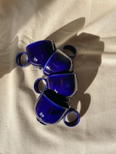 three blue coffee cups sitting on top of a white sheet with shadows coming from them