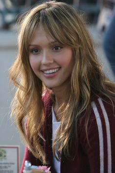 a young woman with long hair is smiling at the camera and holding a cupcake in her hand