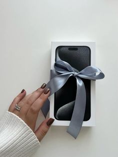 a woman's hand is holding an iphone in a box with a gray ribbon