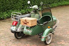 a green scooter with a basket on the back parked in front of a hedge