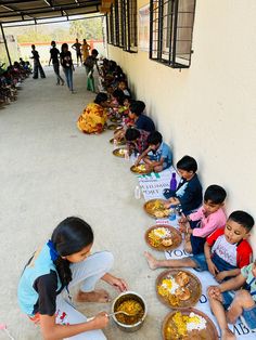 a group of children sitting on the ground with food in bowls and plates next to them