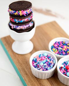 there are four desserts in small white bowls on the wooden tray with sprinkles