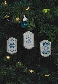 three cross stitch ornaments hanging from a christmas tree with gold stars and blue baubles