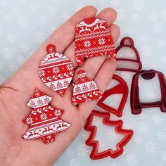 a hand holding some red and white christmas decorations next to two cookie cutters with snowflakes on them