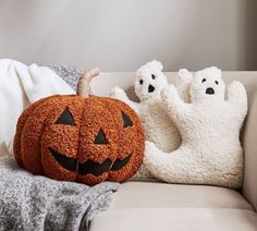 two pumpkins sitting on a couch with ghost pillows