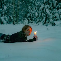 a woman laying in the snow holding a lit candle up to her face with both hands