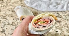 a hand holding a wrap filled with meat and veggies on top of a counter