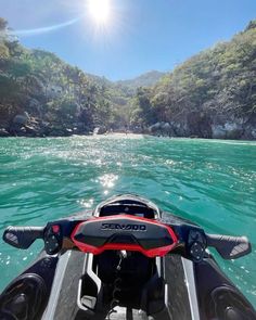 the back end of a boat in clear blue water with mountains in the background and sun shining