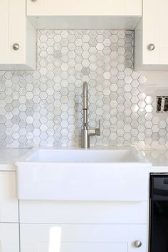 a white kitchen with hexagonal tiles on the backsplash and stainless steel faucet