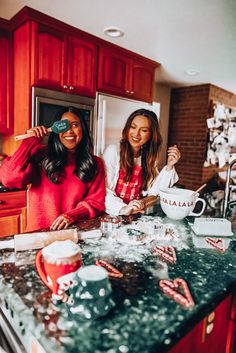 two women are in the kitchen making christmas cookies and smiling at the camera while one woman is holding a spoon