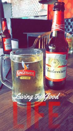 two beer bottles sitting next to each other on top of a wooden table with the words living the good life written across it