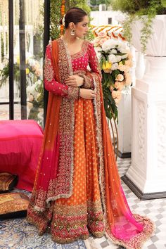 a woman in an orange and pink lehenga standing next to a flower arrangement