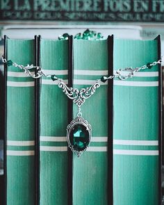 a green book with a necklace on it sitting in front of a stack of books