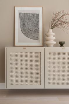 a white cabinet sitting next to a vase on top of a wooden table in front of a painting