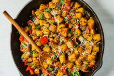 a skillet filled with potatoes and vegetables on top of a white countertop next to a wooden spoon