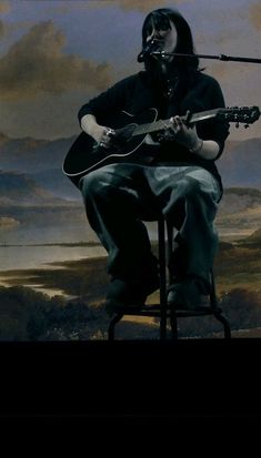 a man sitting on top of a chair holding a guitar in front of a painting