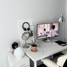 a white desk with a computer and headphones on it, next to a potted plant