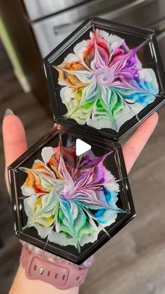 two clear boxes with colorful flowers in them on the palm of someone's hand