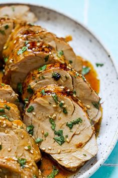 a white plate topped with sliced pork covered in sauce and garnished with parsley