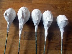 four pieces of white paper are lined up on a wooden table with toothpicks sticking out of them