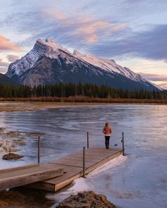 a woman standing on a dock in front of a mountain