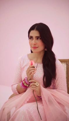 a woman sitting on top of a chair holding a pink flower in her right hand